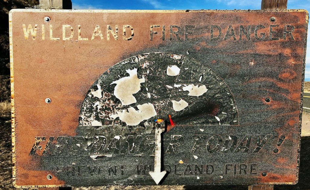 a wild land Fire Danger sign, severely damaged by fire, with burn marks obscuring most of the text 
